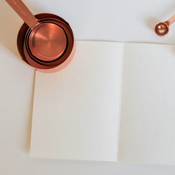 Copper measuring cups and measuring spoons laid on a sheet of white paper