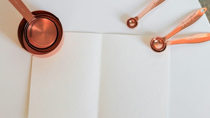 Copper measuring cups and measuring spoons laid on a sheet of white paper