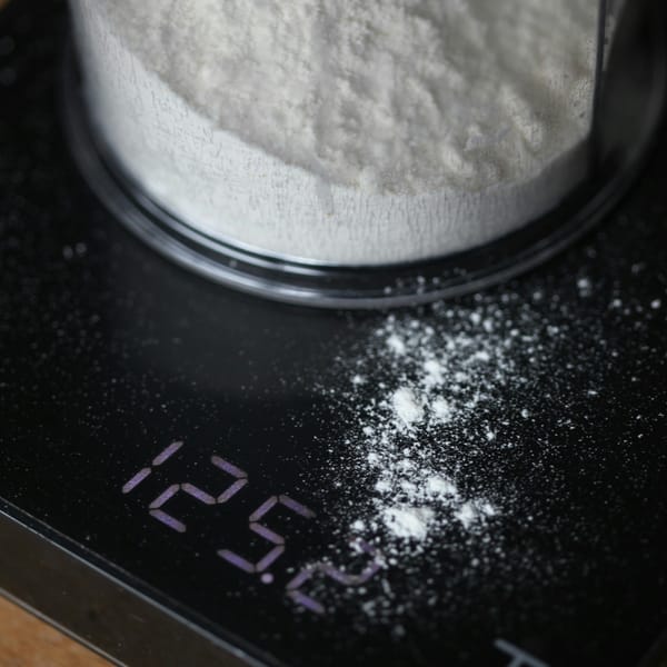 Container of white flour on a black digital kitchen scale showing 125.0